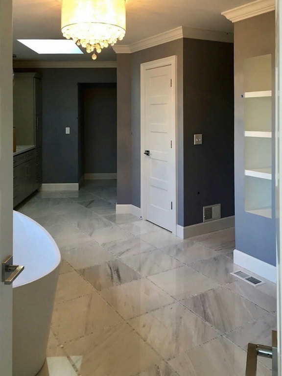 Expansive Carrera Marble Tiled Master Bathroom with Elegant Freestanding Tub, Contemporary Lighting, and Custom Cabinetry Accommodating a Quartz Countertop Built Exclusively by Morgan Homes of Western New York, Inc.
